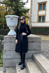 a lady in a black slim sweater, a pair of grey shorts and a black coat